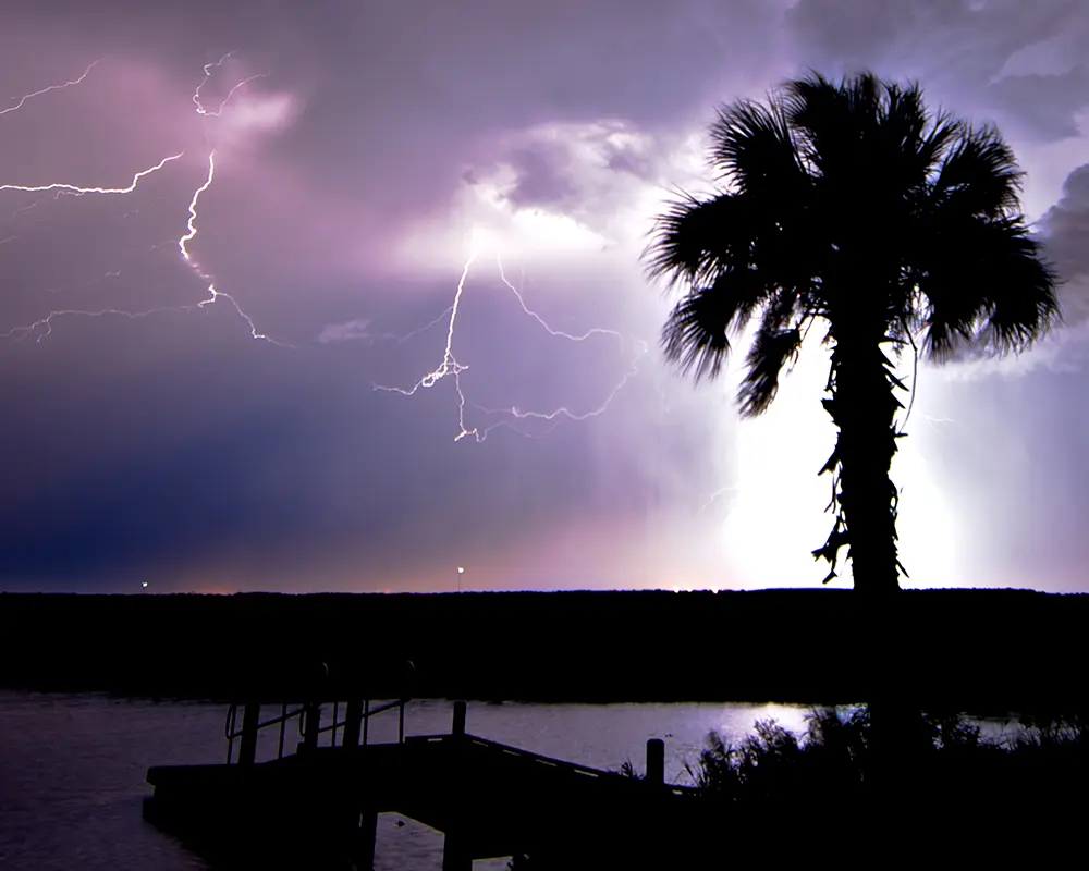 Preparing Your Marine Structures for Hurricane Season in Florida. Featuring a photo of a storm off the coast of Florida, with a palm tree and dock in silhouette.