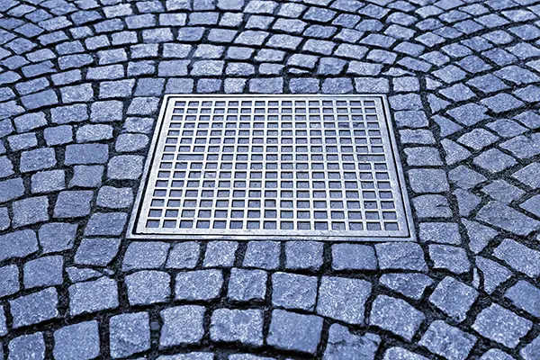 Catch basin with a metal grate installed in a blue cobblestone paver driveway.