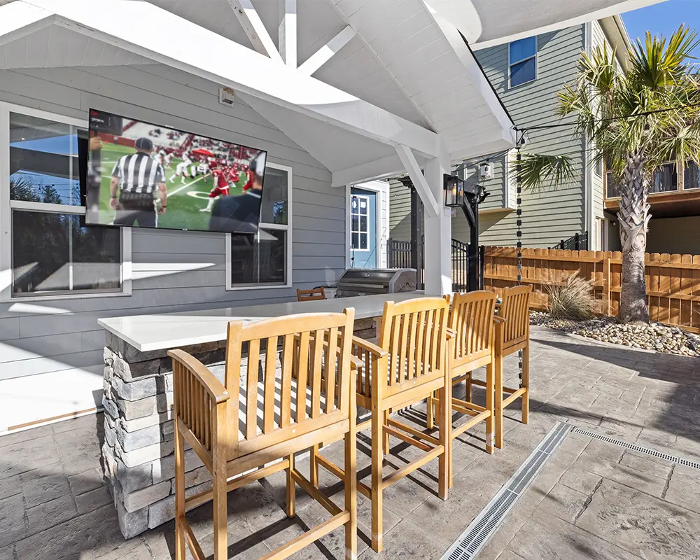 How to Create the Ultimate Outdoor Gameday Setup in Southwest Florida. Featuring a photo of a backyard patio with an outdoor kitchen and a flatscreen TV.